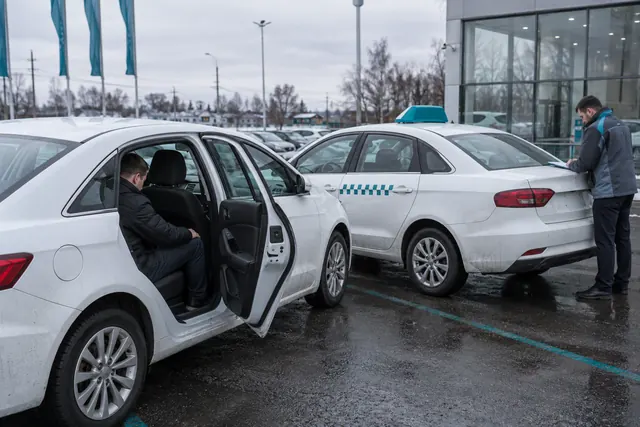 Авто для такси: водитель проверяет место на заднем сиденье белого седана у дилера, рядом седан с фонарём такси