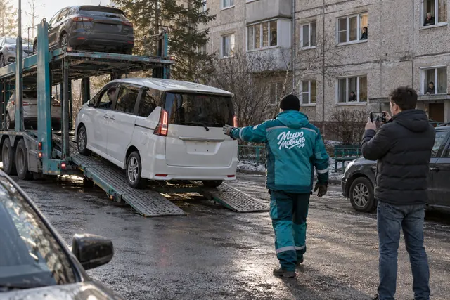 Купить авто с доставкой из Японии: минивэн съезжает с автовоза во дворе дома, сотрудник МироМобиля направляет выгрузку