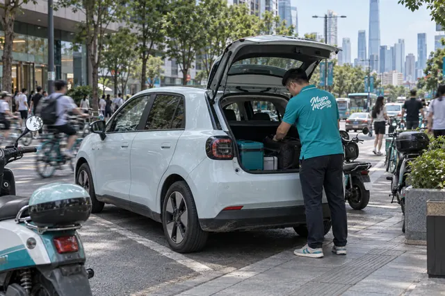 BYD Seagull: сотрудник МироМобиля заглядывает в багажник маленького белого электрохэтчбека на улице китайского города